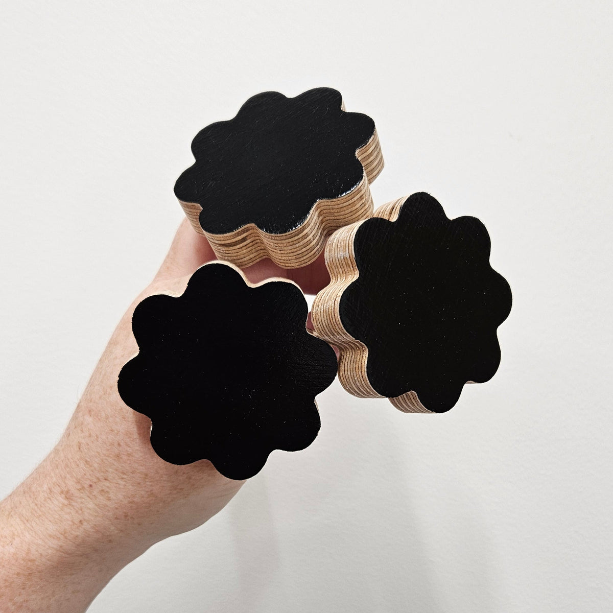 Hand holding a wooden 8 petal flower hook on a light gray background