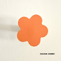 An orange coloured flower-shaped wall hook mounted on a white wall, with the text 'COLOUR: Sorbet' at the bottom.